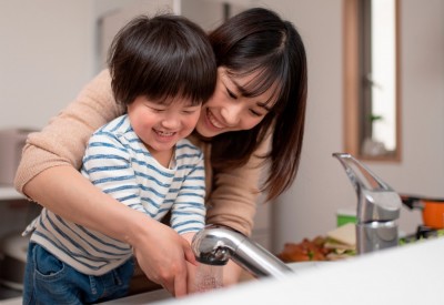 Smiling mother with arms around toddler helping her wash hands at sink Smiling mother with arms around toddler helping her wash hands at sink